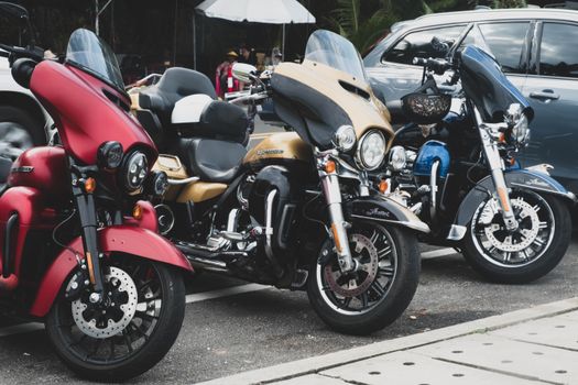 Three motorcycles in vibrant colors parked on a city street with vehicles in the background.