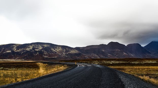 A winding road through a mountainous landscape with cloudy skies, showcasing rugged natural beauty.