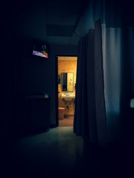 A dimly lit room with a view into a warmly lit bathroom, capturing shadows and light contrast.