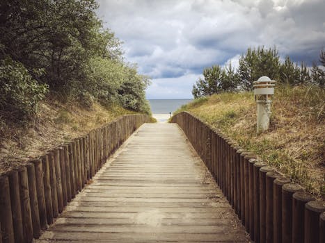 一条宁静的木制小路，被大自然环绕，通往云层密布的天空下的宁静海滩