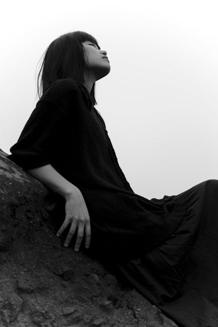 Elegant black and white photo of a woman posing on a rocky surface.