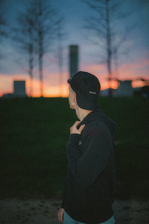 A man in a hat and jacket standing in front of a sunset