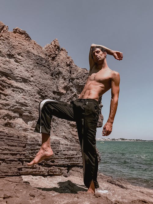 A shirtless man standing on the rocks near the ocean