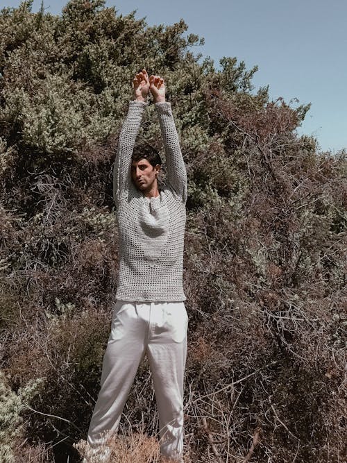 A man in white pants and a grey sweater is holding up his arms