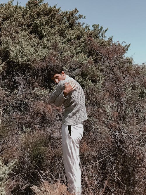 A man in a sweater and pants is standing in the bushes