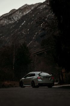A sleek silver sports car drives on a scenic mountain road at dusk.