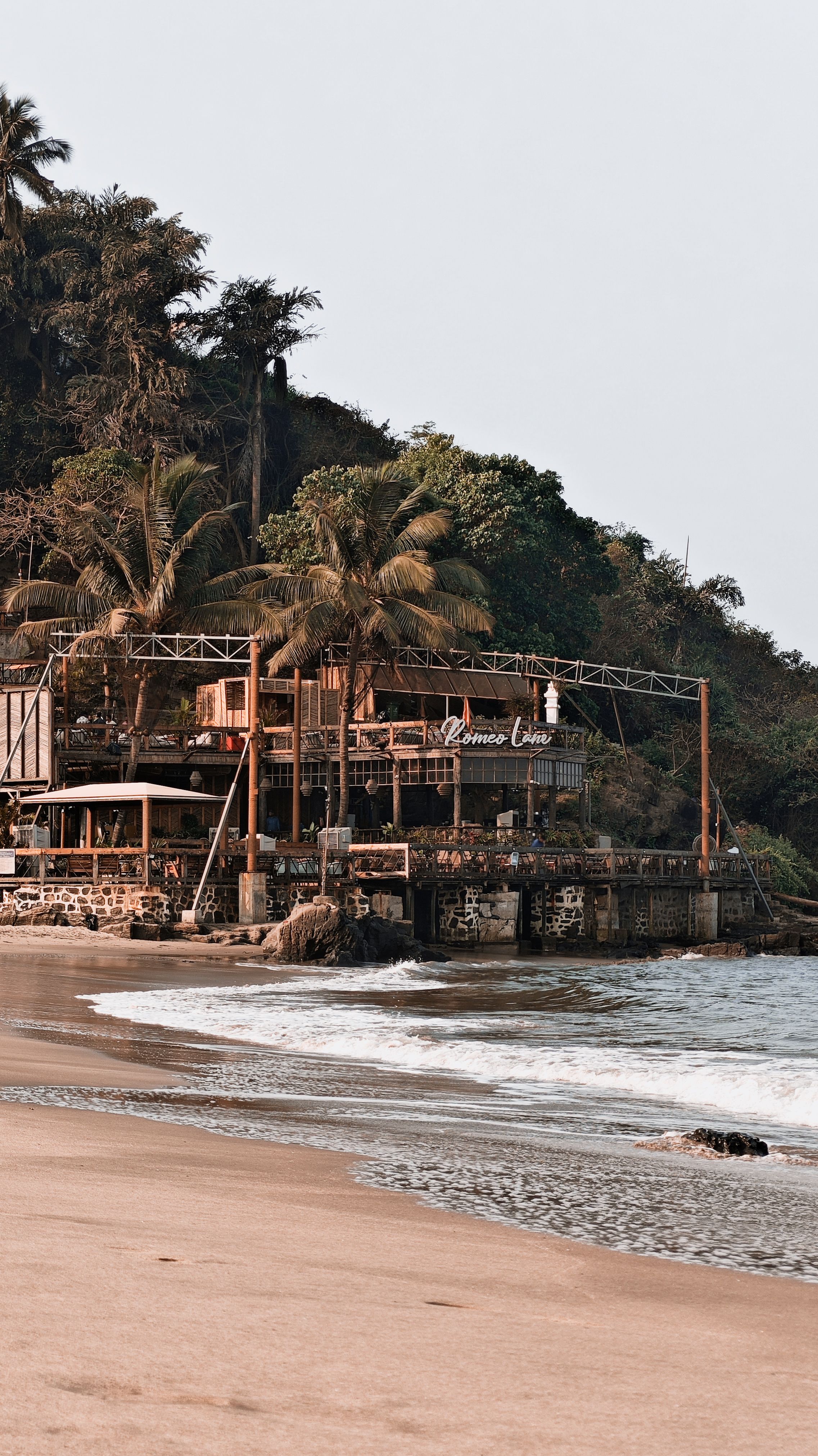 Serene beach view with palm-lined cafe, perfect tropical getaway.