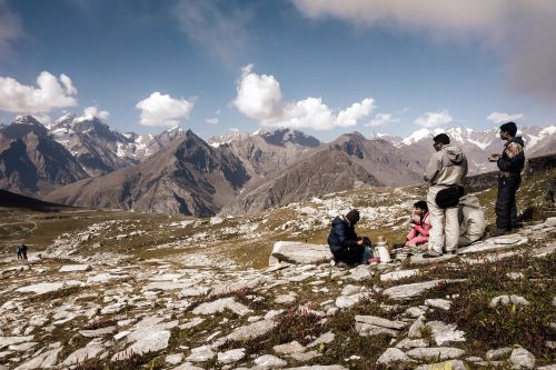 Free People resting on a rocky mountain overlook with majestic snow-capped peaks and blue sky. Stock Photo