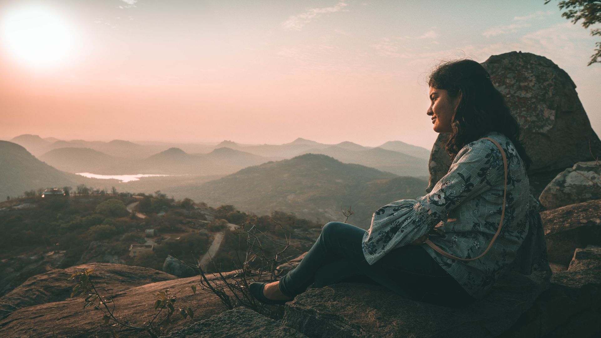 Woman sitting on a rock, looking out over misty mountains at sunset