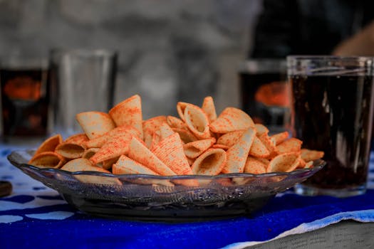 Close-up of spicy seasoned chips in a glass plate with soft drinks beside them.