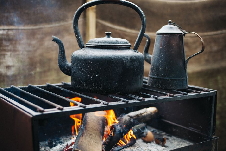 How Electric Kettles with Temperature Control Elevate Pour Over Brewing A vintage iron kettle over an open flame, exuding a rustic and warm outdoor ambiance.