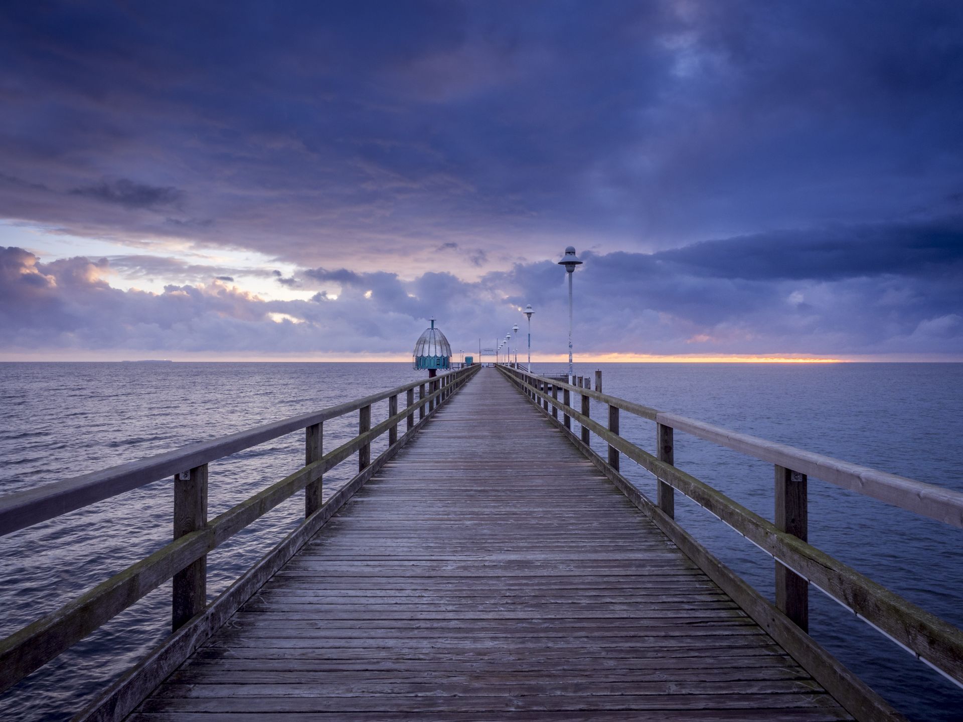 A peaceful pier stretches into the Baltic Sea under a vivid sunset sky, capturing serene coastal beauty.