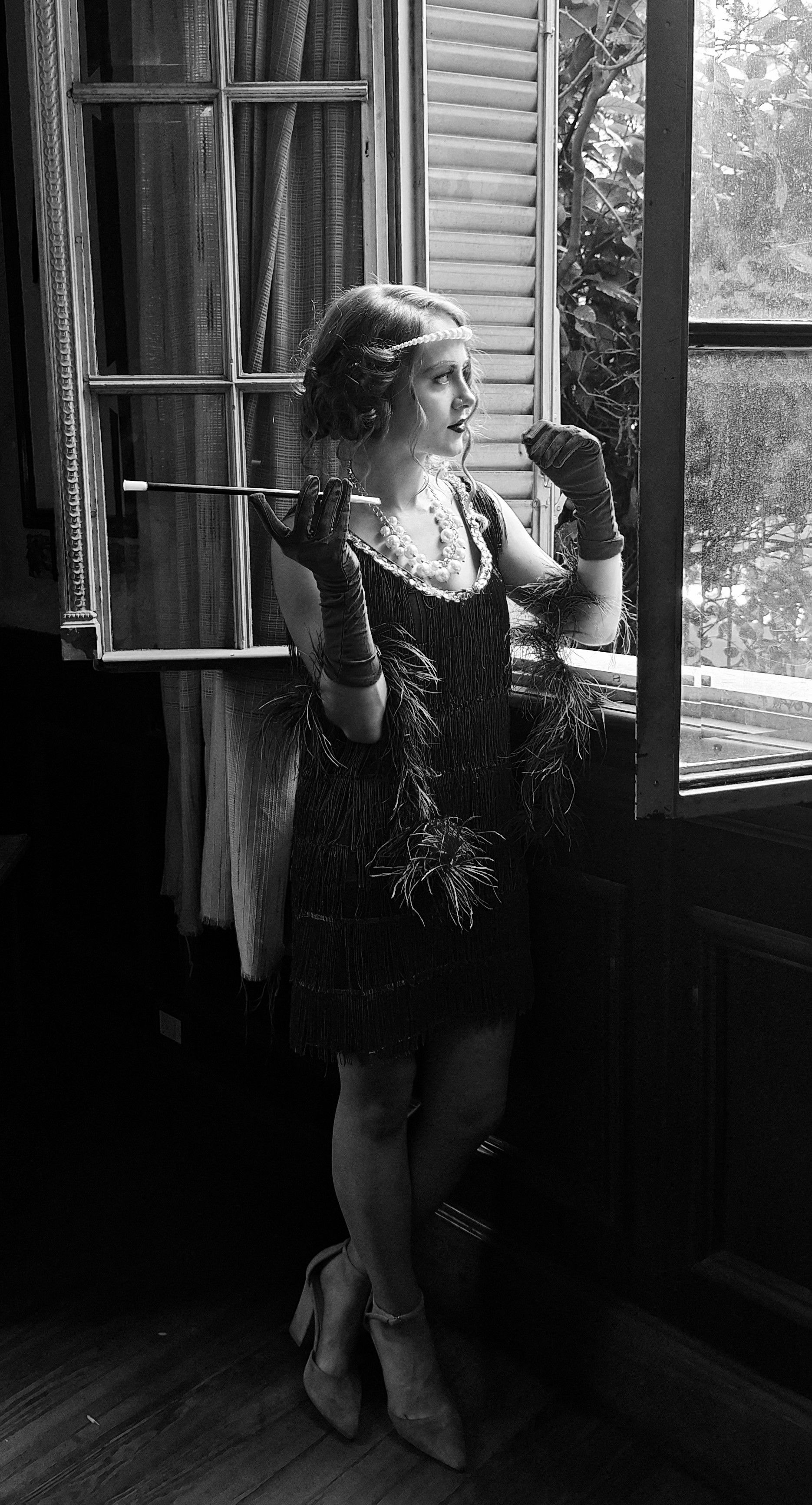 A woman in a vintage flapper dress posing elegantly near a window, exuding retro charm.