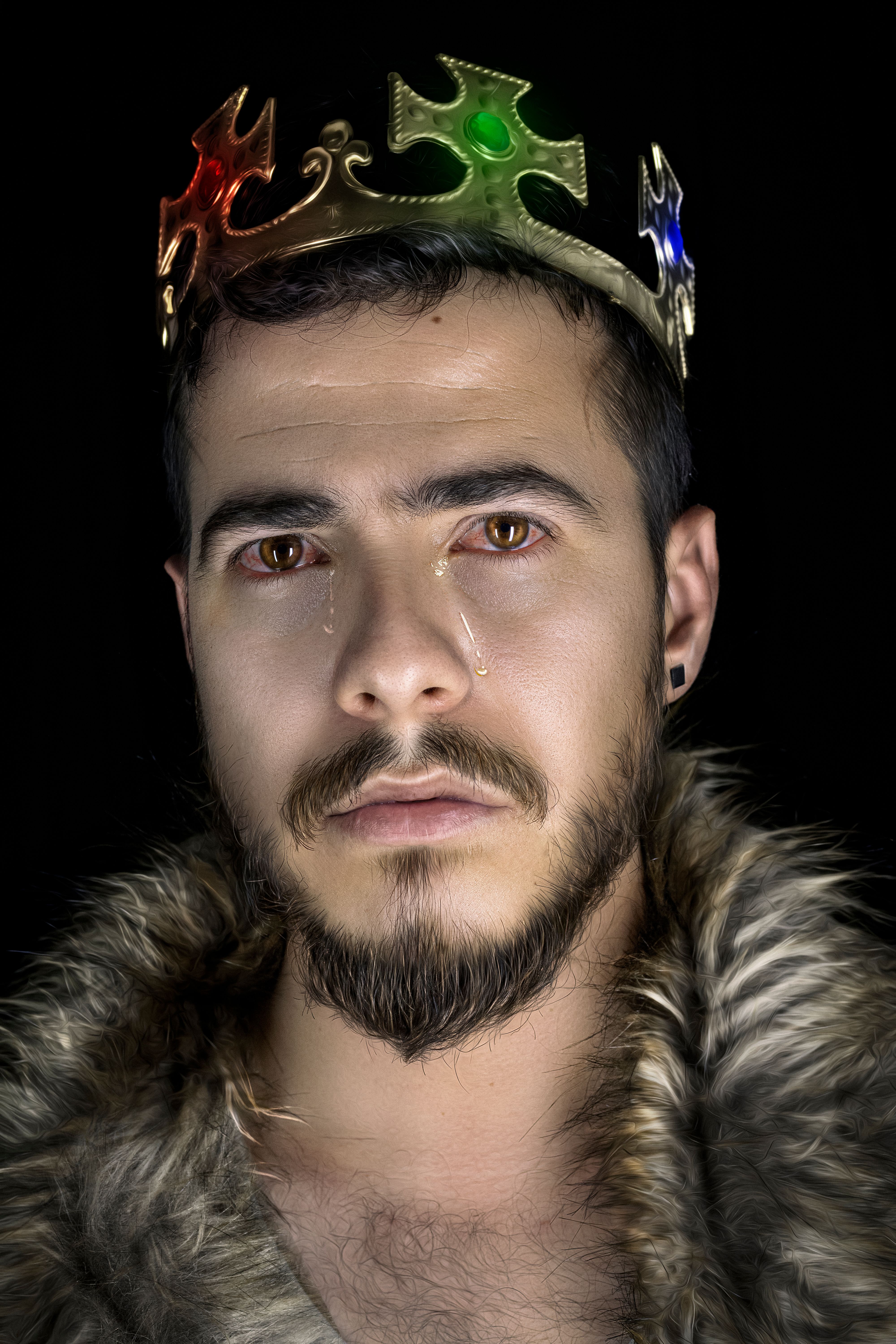 Close-up portrait of a man wearing a jeweled crown and fur coat, expressing emotion.