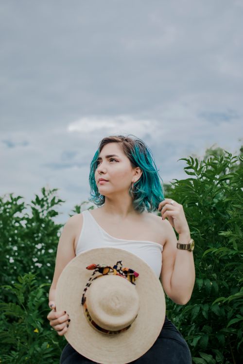 Free Stylish young woman with blue hair in a natural outdoor setting holding a straw hat. Stock Photo
