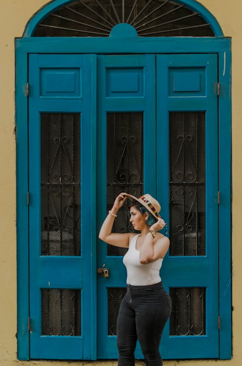 Woman Standing Near Blue Door While Holding Her Hat