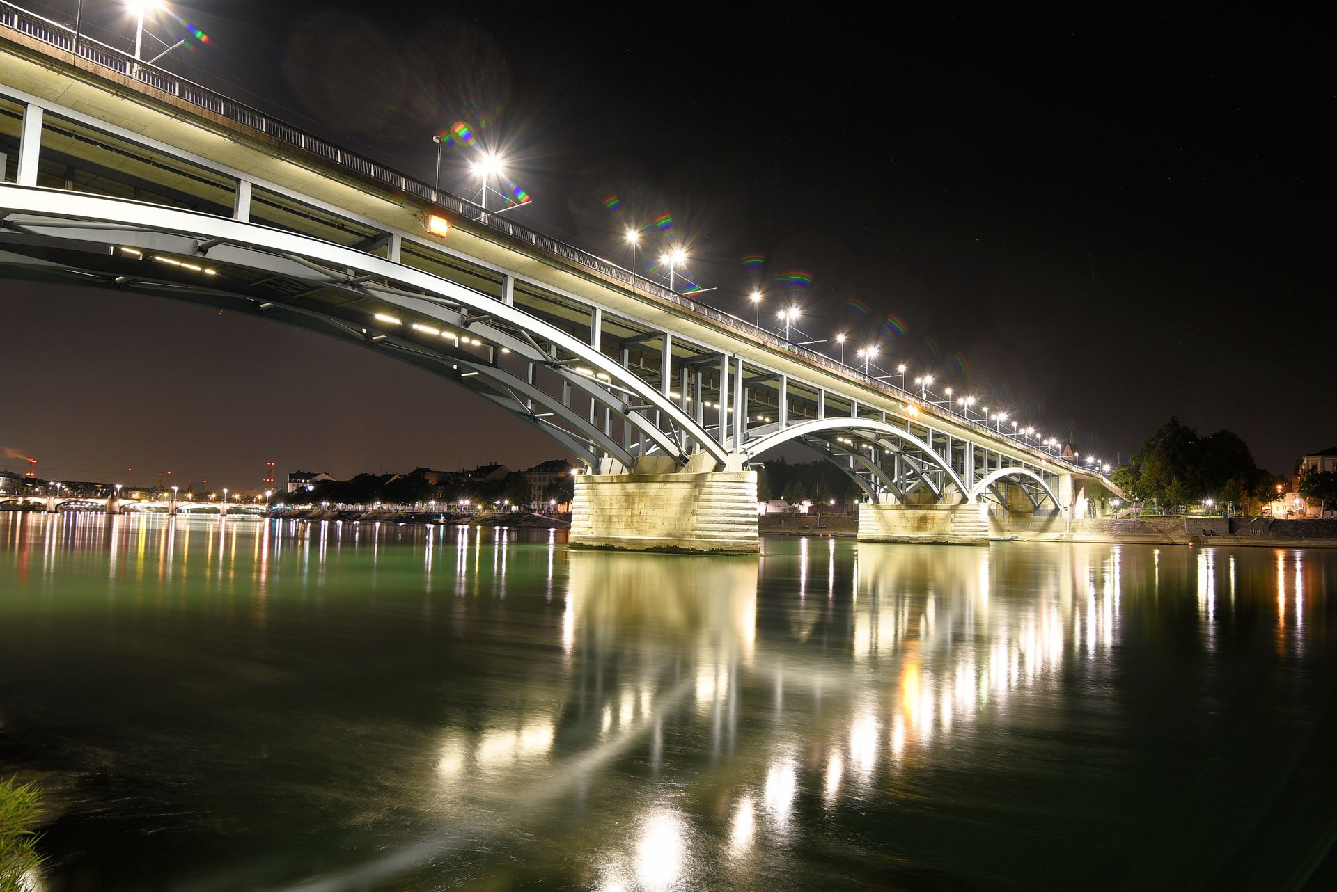 Stunning night-time view of an illuminated bridge reflecting over calm waters in an urban setting.