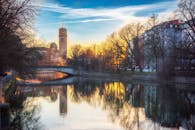 慕尼黑的河畔日落景色中，桥梁、建筑物和树木倒映在水中