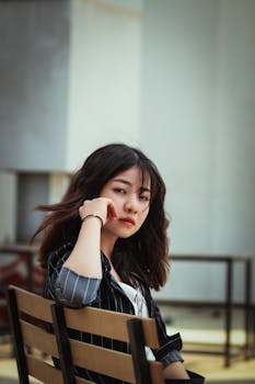 一位年轻女子坐在户外，背景是现代城市，她看起来若有所思