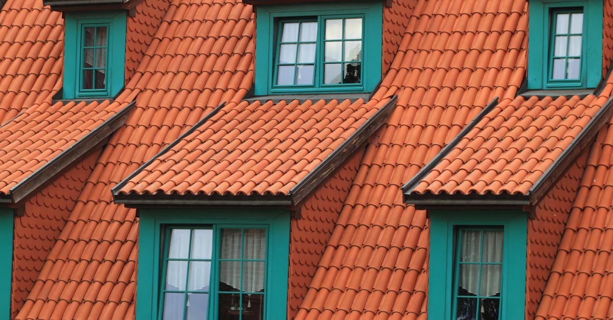 Close-up of an orange tiled roof with green framed dormer windows, creating a colorful architectural contrast.