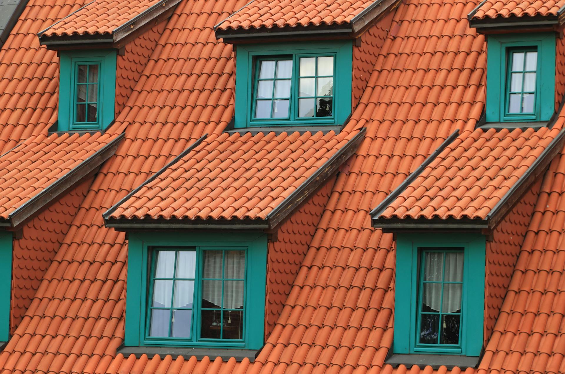 Close-up of an orange tiled roof with green framed dormer windows, creating a colorful architectural contrast.