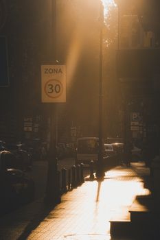 Golden sunlight casts shadows on an urban street with traffic signage and parked cars, creating a warm ambiance.