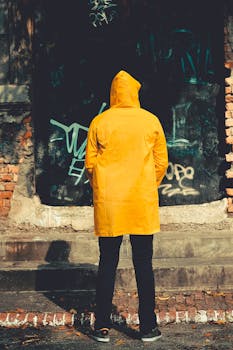 一个穿着黄色雨衣的人站在涂鸦的砖墙上，背景是城市街道风格