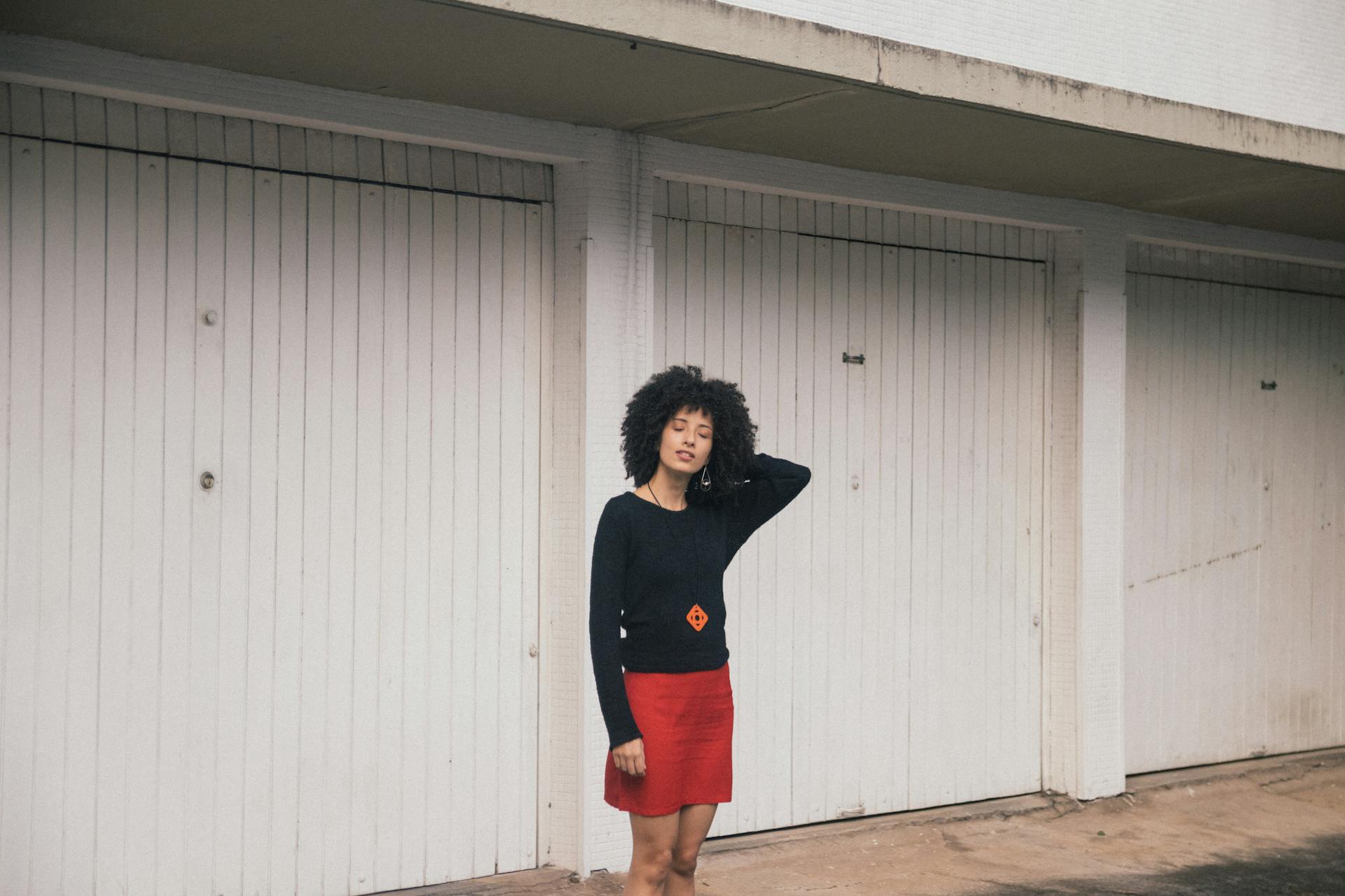 Fashionable woman in red skirt and black top posing outdoors with white garage doors in São Paulo.
