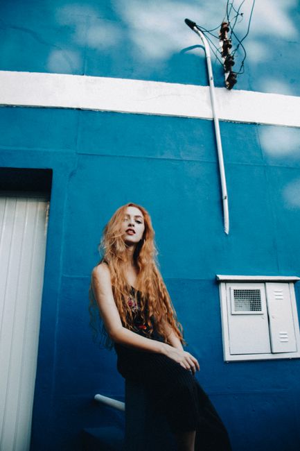 Stylish woman with long hair posing in front of a vibrant blue wall, showcasing fashion and individuality.