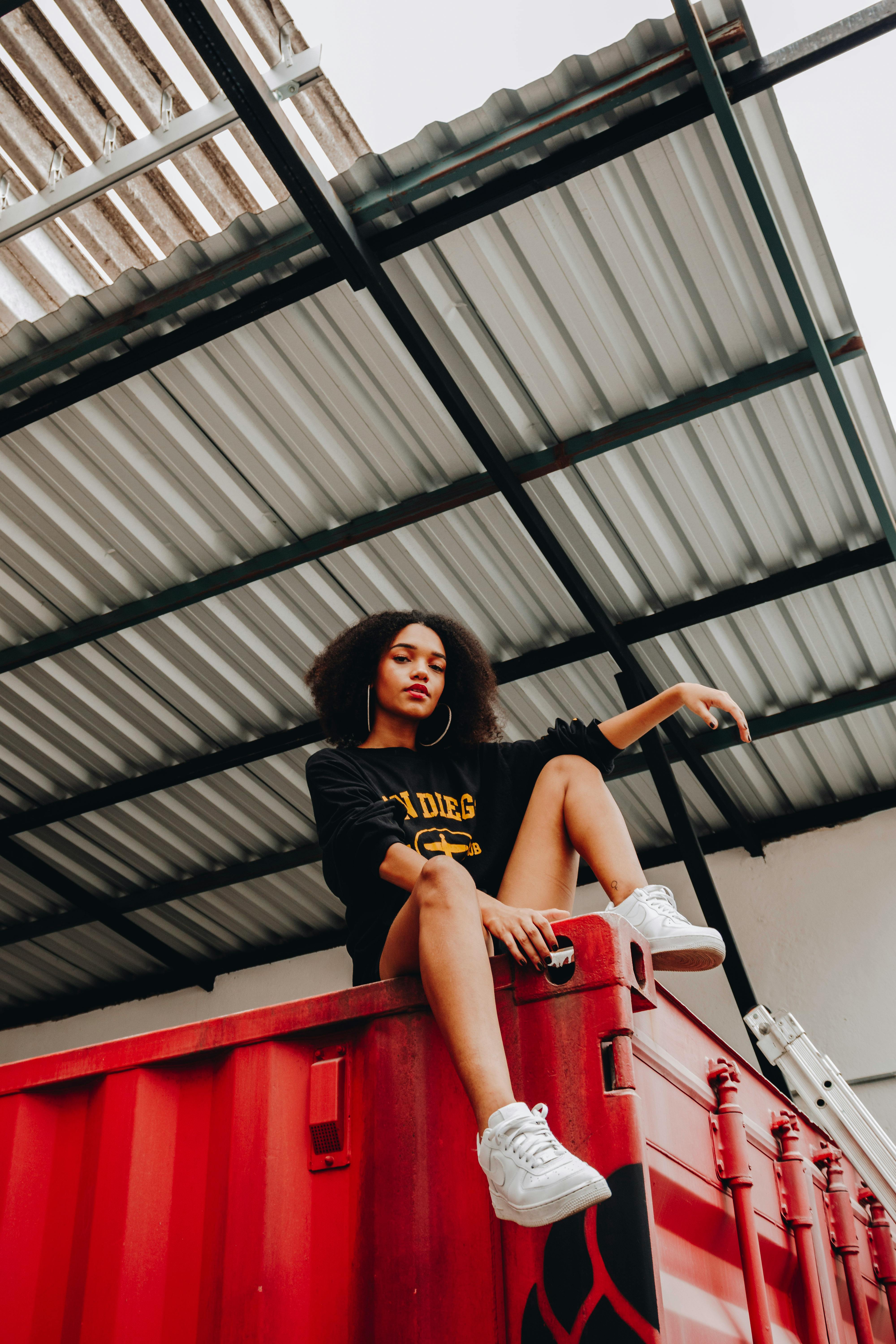 Stylish woman poses atop a red container in a modern urban setting.