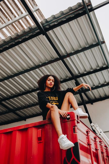 Stylish woman poses atop a red container in a modern urban setting.