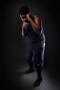 Focused boxer in athletic stance on dark background, showcasing intensity and power.
