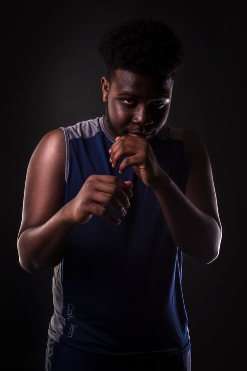Free A young African American boxer poses confidently in a dark studio setting, ready for action. Stock Photo