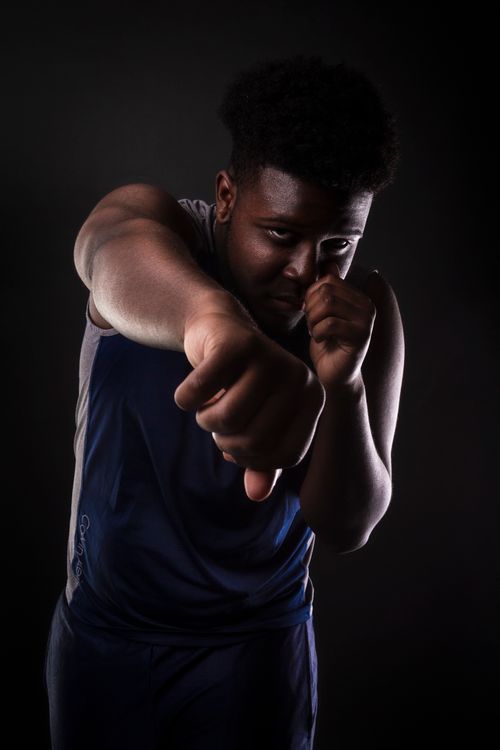 Free Dynamic portrait of a strong African American boxer throwing a punch in a dark studio. Stock Photo