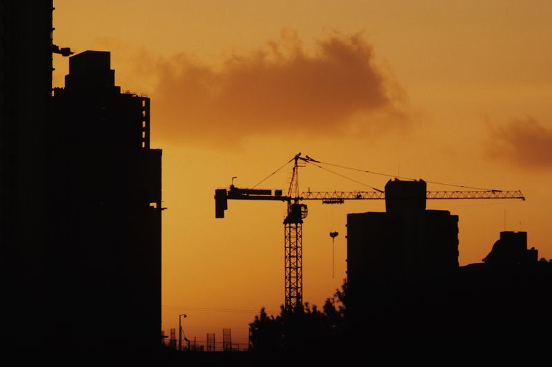 Silhouette of cranes and buildings against a vibrant sunset sky.