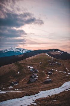 黄昏时分，白雪皑皑的山峰下，风景如画的山村显得格外宁静