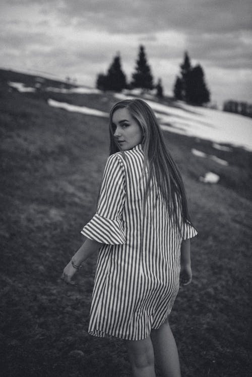 Grayscale Photo of Woman in Striped Dress Walking on Hill Slope With Snow While Looking Back