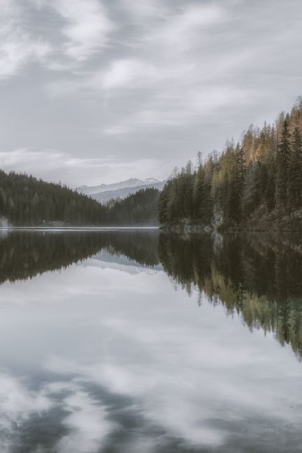 A tranquil mountain lake reflecting surrounding forests under a cloudy sky.