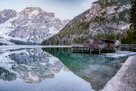 宁静的冬日景致，白雪皑皑的山脉与湖边小屋，倒映在平静的高山湖泊中