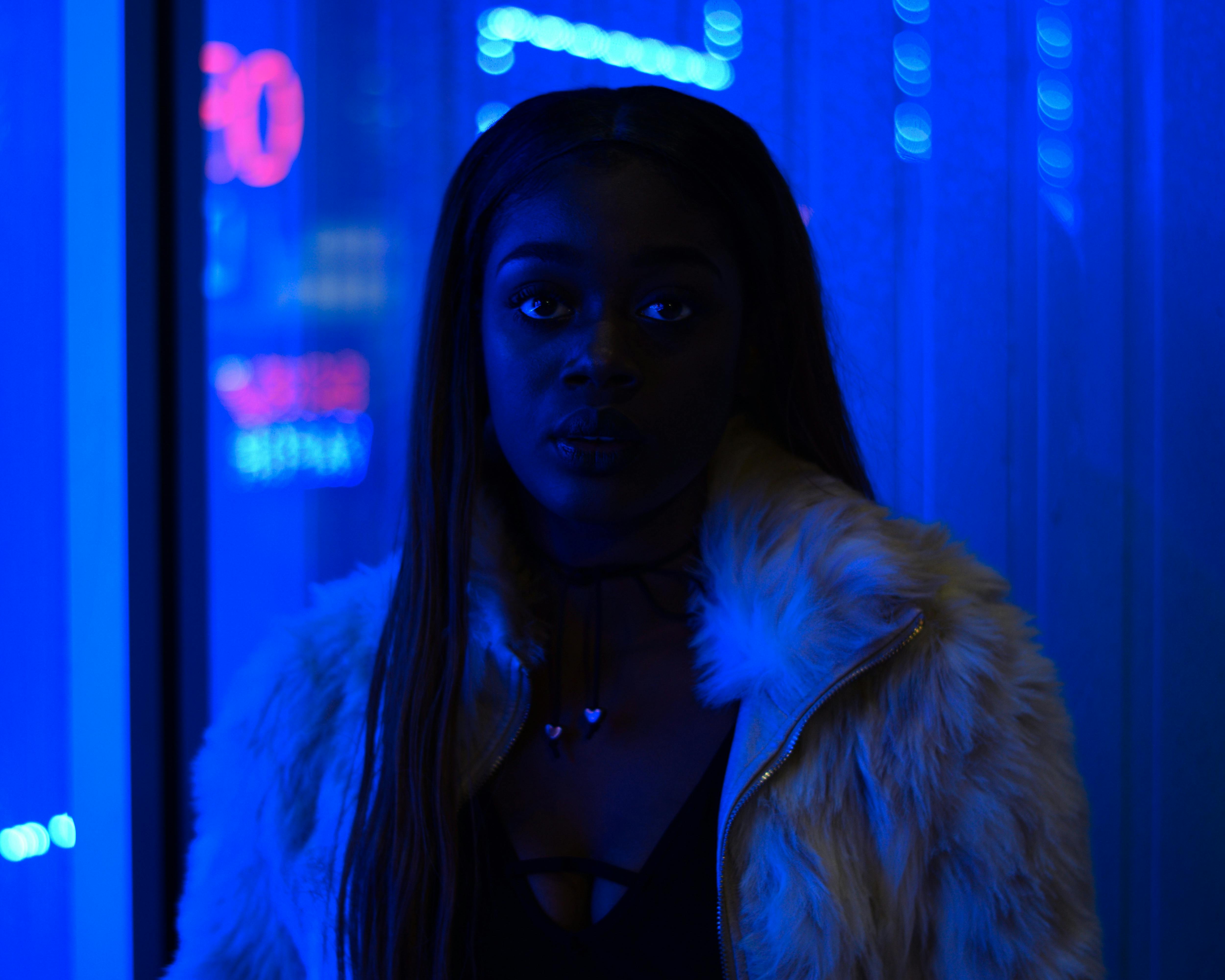 Striking portrait of a woman in a fur coat under moody blue LED lights.