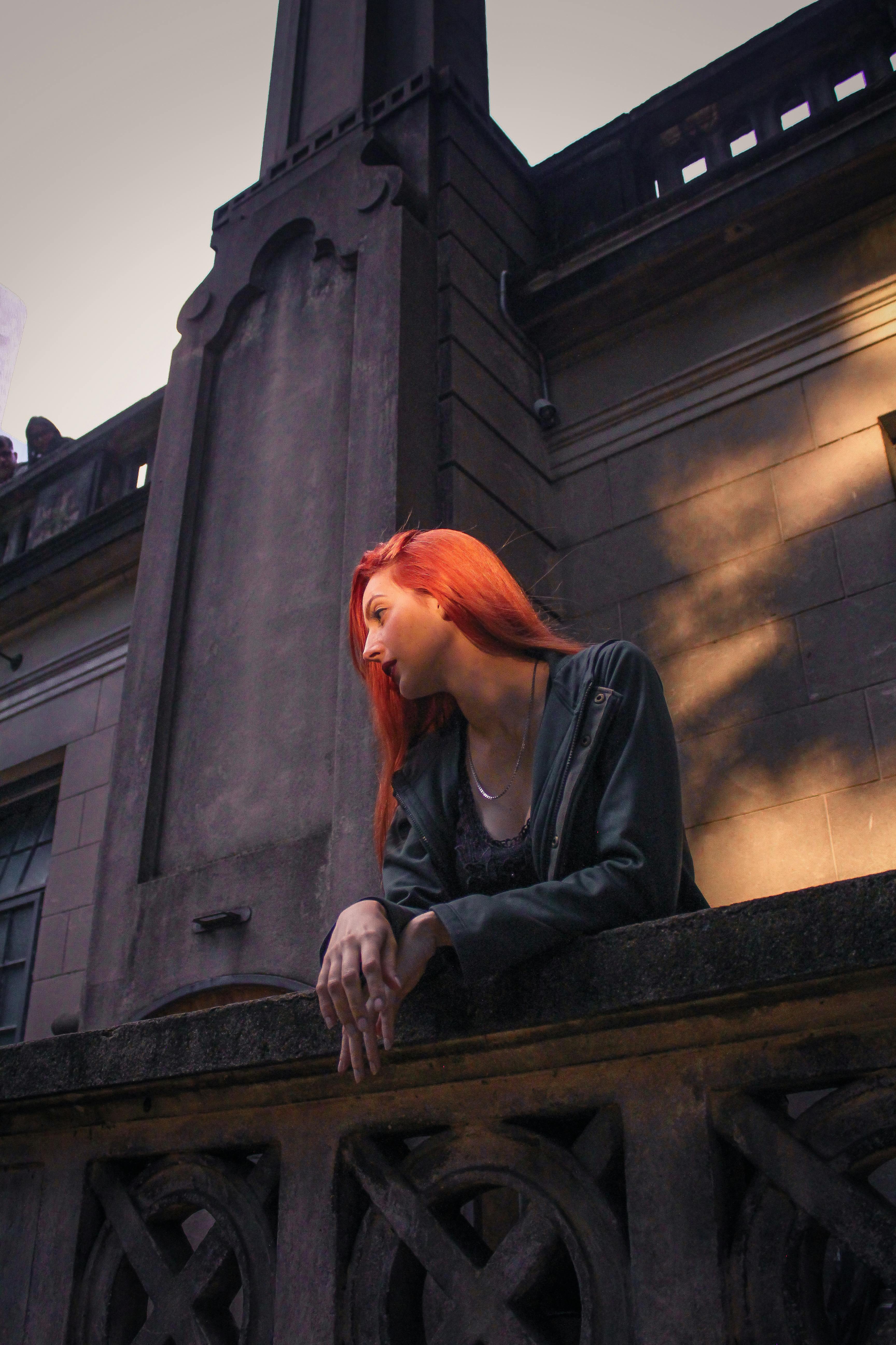 一名红发鲜艳的妇女靠在历史建筑立面的石栏杆上