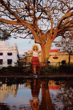 一名身穿彩色裙子的女子在公园的树旁摆姿势，水中映出倒影