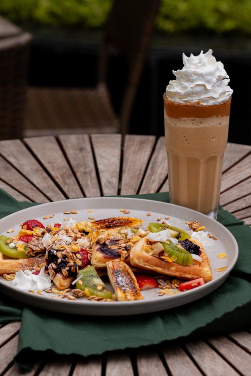 Free Mouthwatering waffles topped with fresh fruits and cream next to an iced coffee with whipped cream. Stock Photo