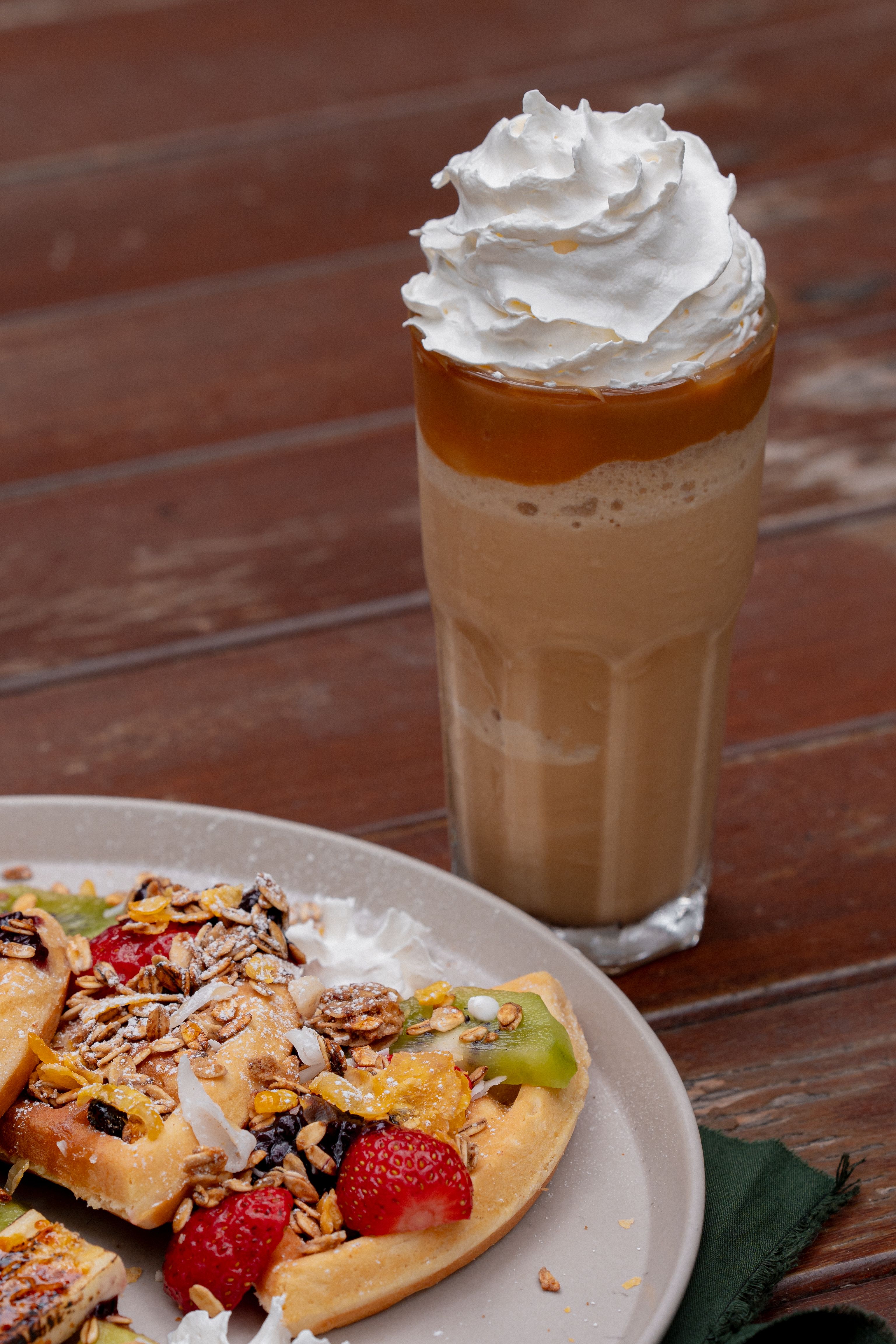 A glass mug of butterbeer with amber-colored soda topped with swirled whipped cream and a drizzle of butterscotch sauce.
