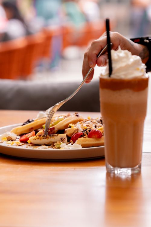 Free Close-up of waffles with fruit and cream served with a tall glass of iced coffee in a cozy café setting. Stock Photo