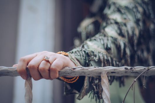 A close-up shot of a person's hand wearing a ring, resting on a weathered rail. Soft focus background.
