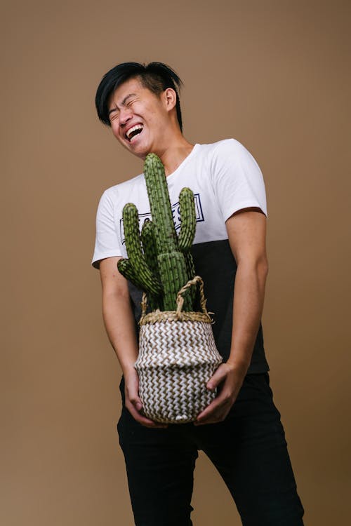 Free Man in White and Black Shirt Holding Pot With Cactus Plant Stock Photo