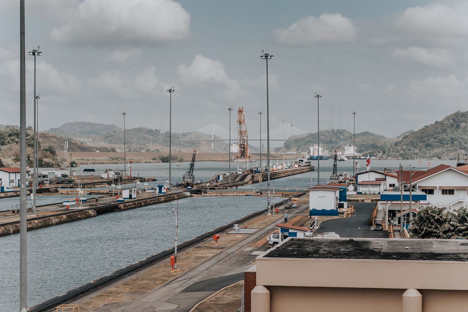 Empty Panama Canal lock chambers with control buildings and a cable-stayed bridge in the hills behind