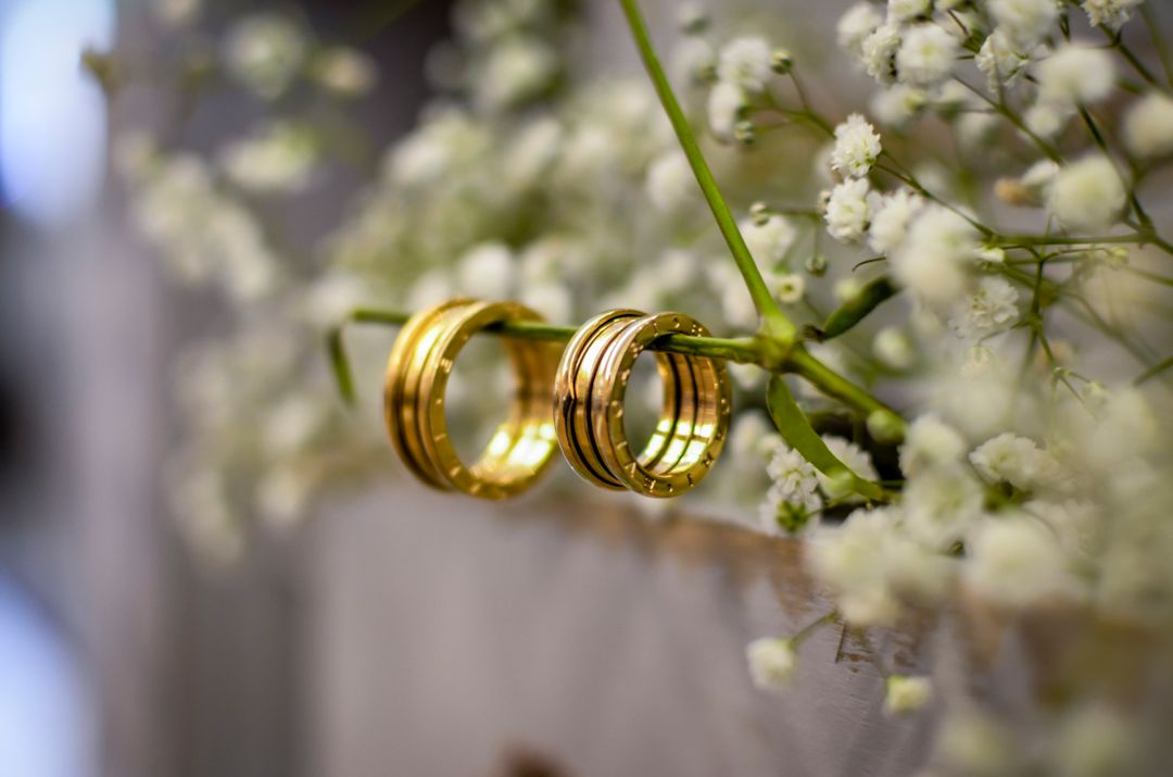 engagement ring vs wedding ring for men — two patterned gold wedding bands hanging from baby's breath flowers — FoundryCut