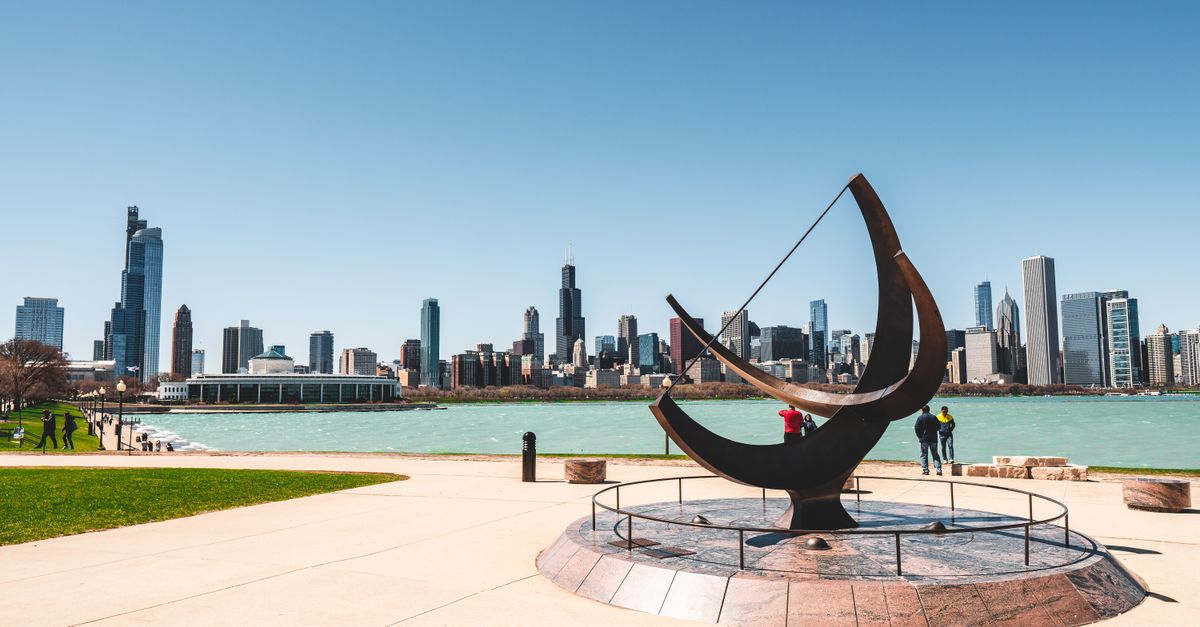 A scenic view of Chicago skyline from the waterfront with modern architecture and a striking sculpture.